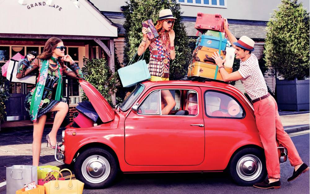 A small red car with suitcases and shopping on the roof
